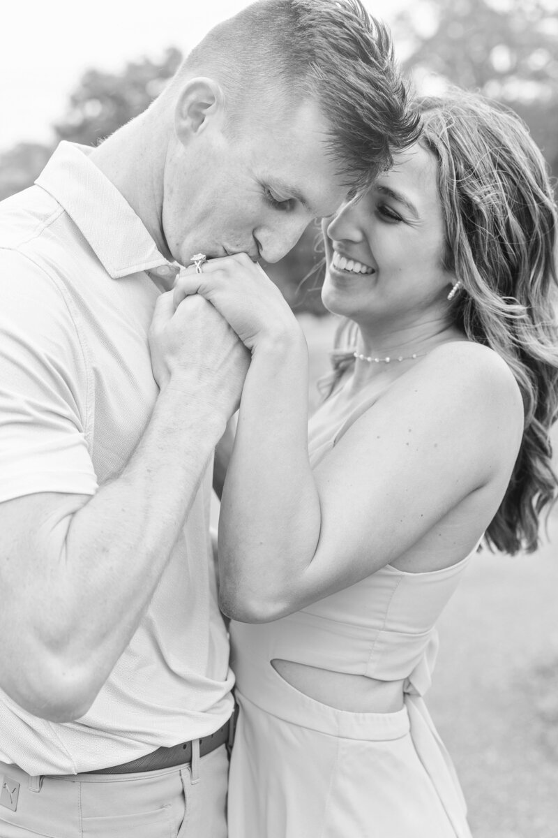 Black and white photo of a man kissing his fiancée's hand with her engagement ring visible, both smiling