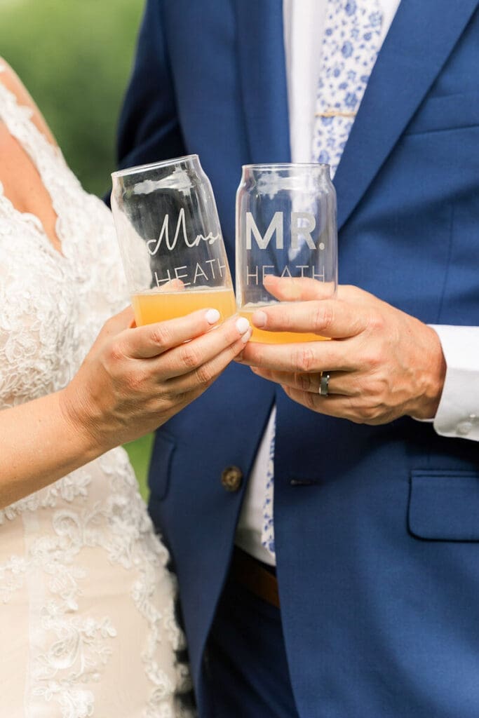 Bride and groom toasting with etched glasses reading "Mrs. Heath" and "Mr. Heath," groom in a blue floral tie