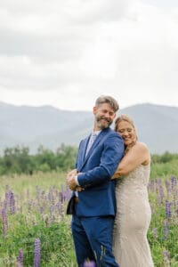 Bride and groom embracing with eyes closed among purple lupines with mountains behind in Sugar Hill, New Hampshire