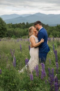 Bride and groom kissing in a field of purple lupines with the White Mountains behind them in Sugar Hill, NH